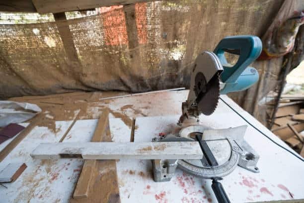 Compact miter saw positioned on a dusty workbench with an aluminum guide piece