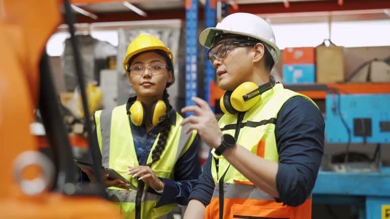 Two quality control personnel wearing PPE engaged in discussion during factory floor inspection process