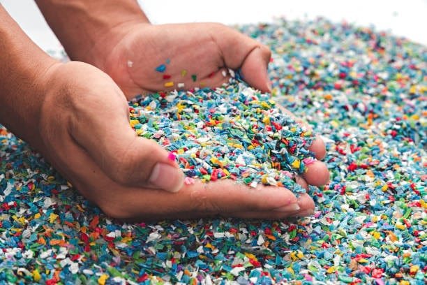 Hands holding shredded multicolor recycled polypropylene flakes, emphasizing sustainability and safety.