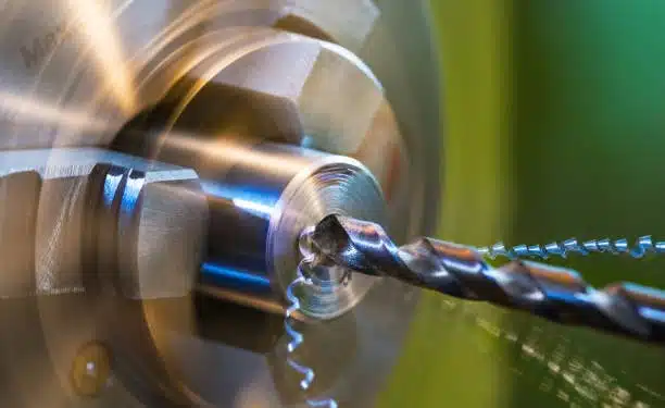 Close-up of rotating CNC chuck with drill bit producing metal chips