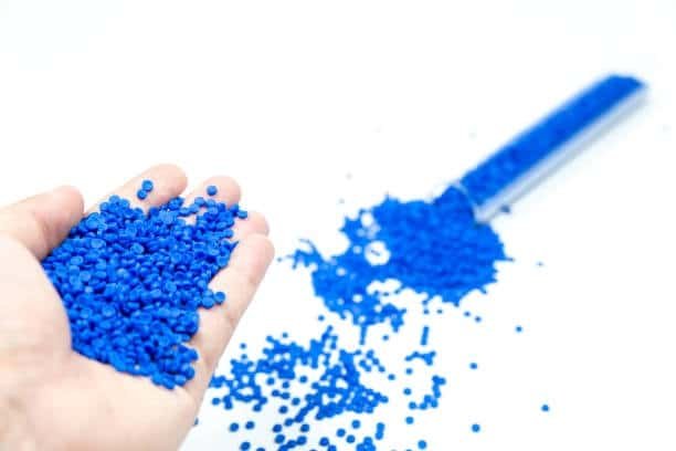 Hand holding blue non-toxic TPE pellets with lab sample spilled in background.