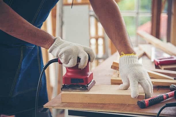 Craftsman smoothing a wooden block with a handheld electric sander