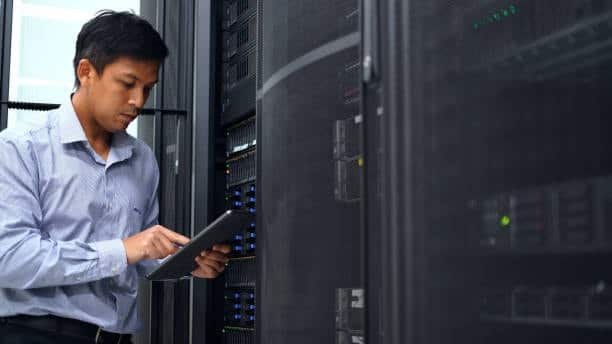 Engineer using a tablet to monitor and configure systems in a high-tech server room