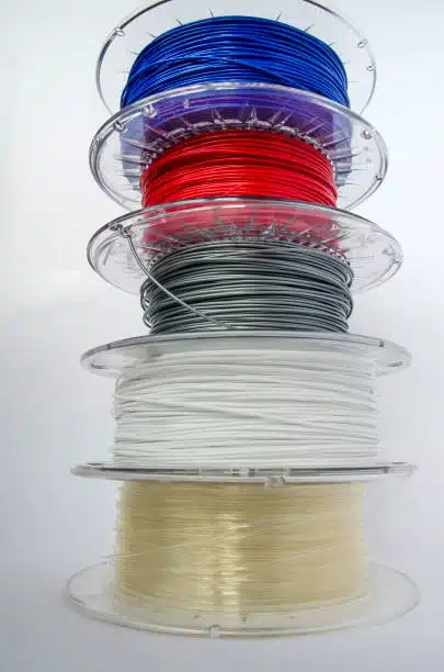 Vertical stack of colorful polycarbonate filament spools showing material variations for printing.