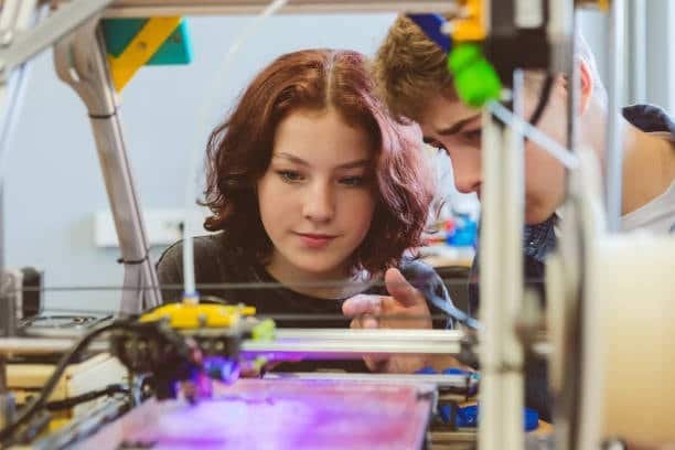 Two students examining a desktop FDM 3D printer during an educational workshop.