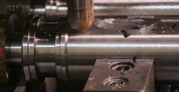 End mill machining a cylindrical metal piece with cutting fluid