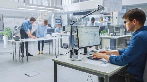 Professional engineer working on CAE project using digital blueprints in an open office.