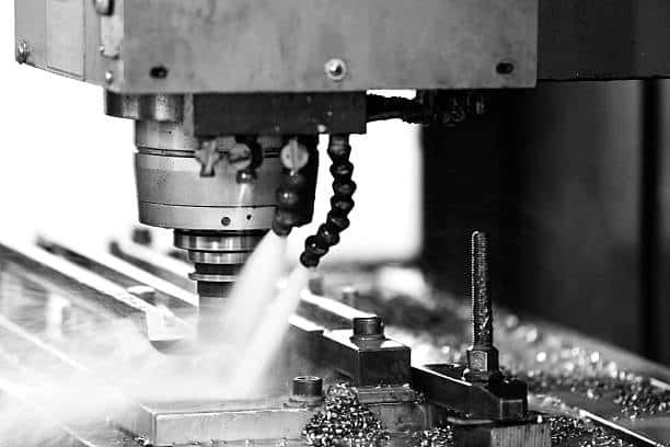 Vertical CNC milling machine cutting metal with visible fluid spray