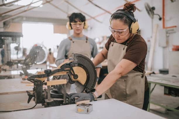 Female technician using a circular saw under supervision in a training workshop environment