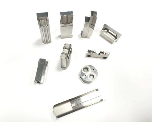 A collection of small, CNC-machined metal mold inserts used for precision packaging injection components, arranged on a white background.