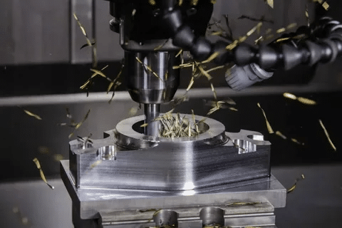 CNC mill removing material from metal part with scattered metal chips.
