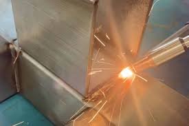 Laser welding torch creating a precision weld on a stainless steel corner joint with visible sparks