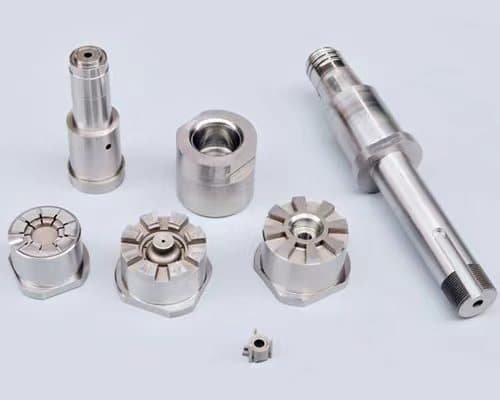 A collection of precision tool steel parts machined by EDM (electrical discharge machining), featuring cylindrical and turret-style geometries with mirror-like finishes