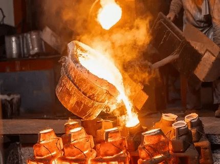 Worker pouring molten metal into sand molds during sand casting process.