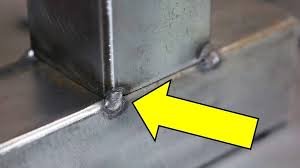 Close-up of a tack weld holding a square steel tube to a base plate with alignment arrow