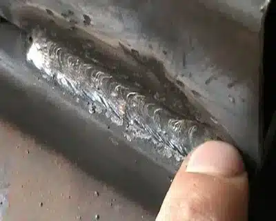 Person pointing to visible weld defect on a metal surface with uneven bead and slag