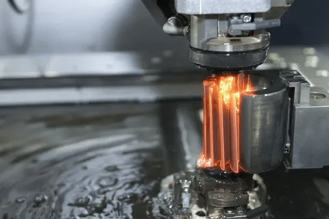 Wire EDM cutting process showing spark erosion as wire electrode slices through metal workpiece submerged in dielectric fluid.