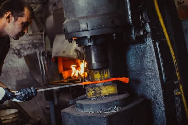 Blacksmith forging long heated metal bar using power hammer