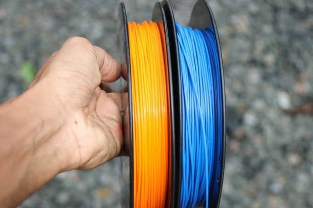 Close-up of orange and blue 3D printer filaments held in hand