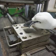 Gloved hand placing raw material charge into a heated compression mold cavity before pressing