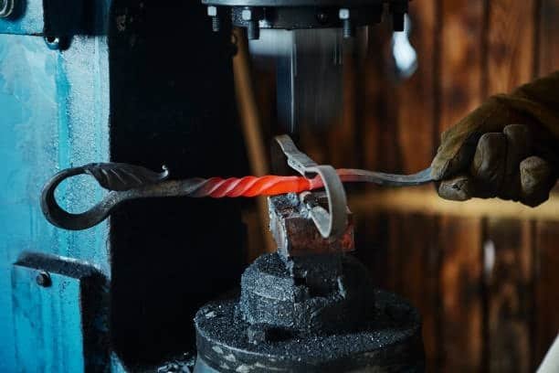 Red-hot twisted metal being shaped under power hammer