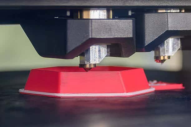 Dual-extruder 3D printer creating red part with precise layering