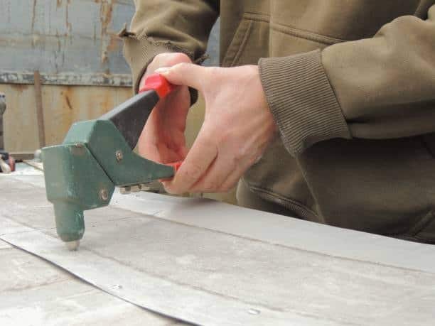 Worker using a manual rivet gun on a metal sheet