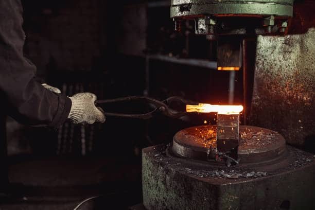 Worker placing red-hot billet under a forging machine for compression