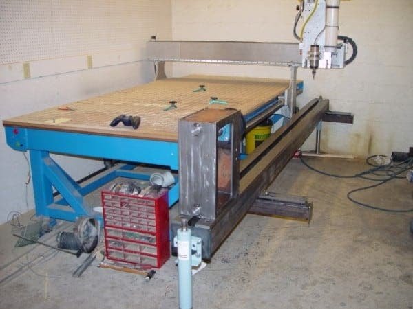 Large-format industrial CNC router with grid-pattern spoilboard and clamps
