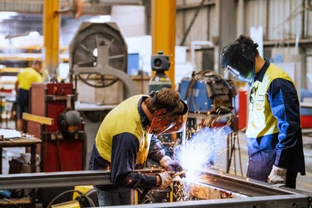 Two factory workers welding a metal frame with sparks flying
