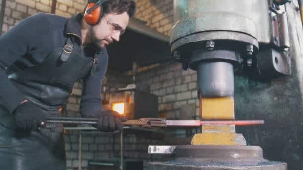 Metal forger shaping heated steel using a hydraulic forging press