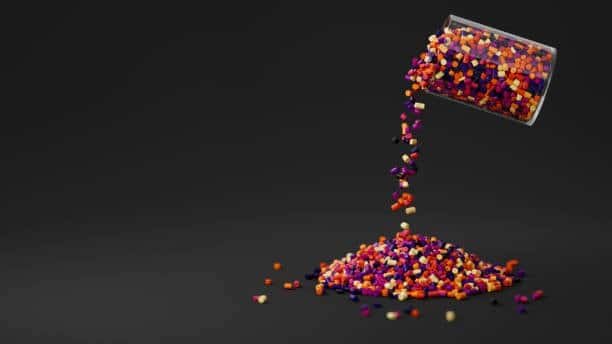 Multi-colored plastic resin granules pouring from a clear container on black background