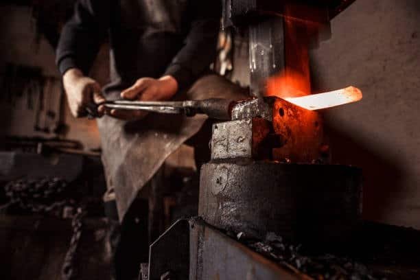 Forging worker hammering a glowing steel rod with hydraulic press