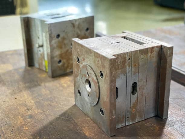 Two steel injection mold blocks resting on a wooden surface before processing