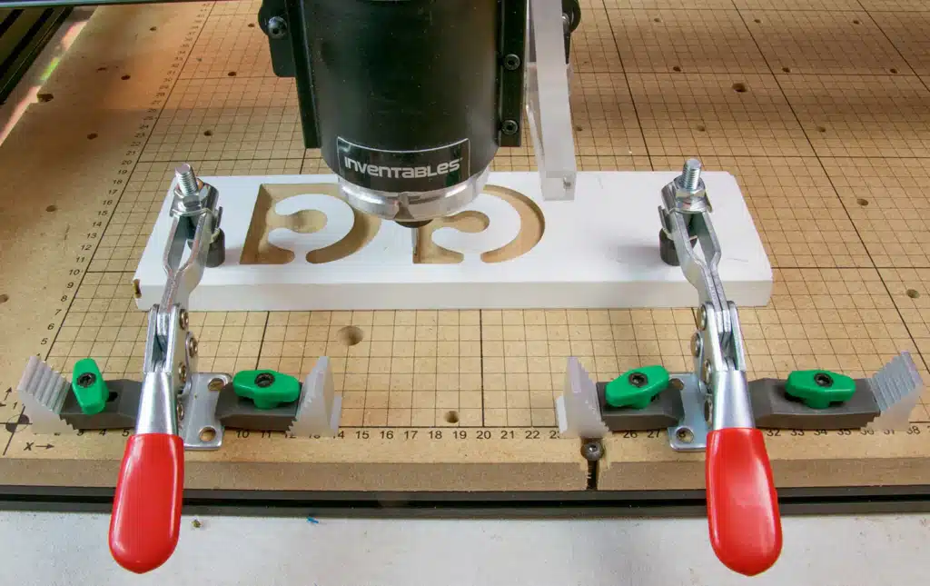CNC router holding a plastic signboard with toggle clamps for accurate engraving