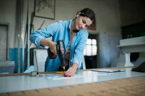 Woman using a power drill on a plastic sheet in a workshop