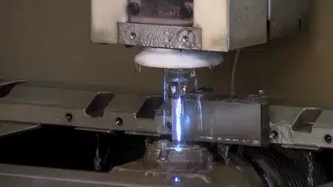 Wire EDM machine cutting metal with dielectric fluid and sparks visible