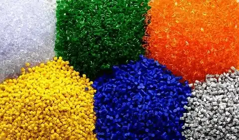 Multicolored thermoplastic pellets including green, blue, yellow, orange, white, and gray, showing raw plastic material for molding and extrusion.