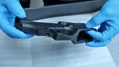 Technician handling a hard anodized aluminum part with protective gloves.