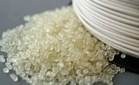 Transparent PLA plastic granules next to white PLA filament for 3D printing