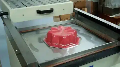 Red plastic product shaped by vacuum forming process cooling on a forming table.