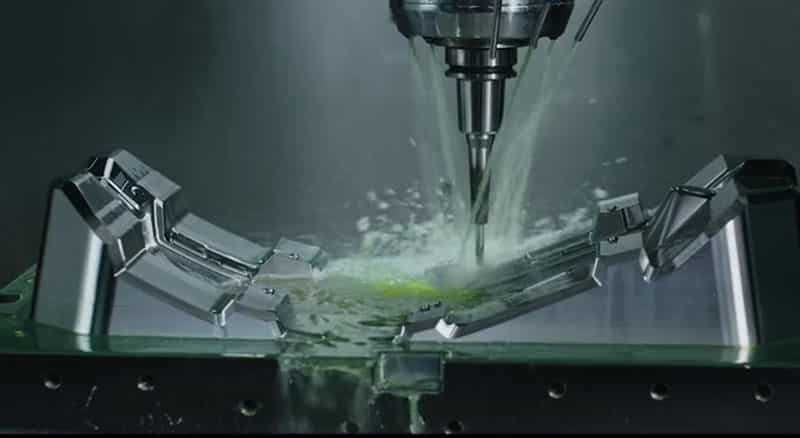 A five-axis CNC machine meticulously cutting a complex mold component with coolant spray.