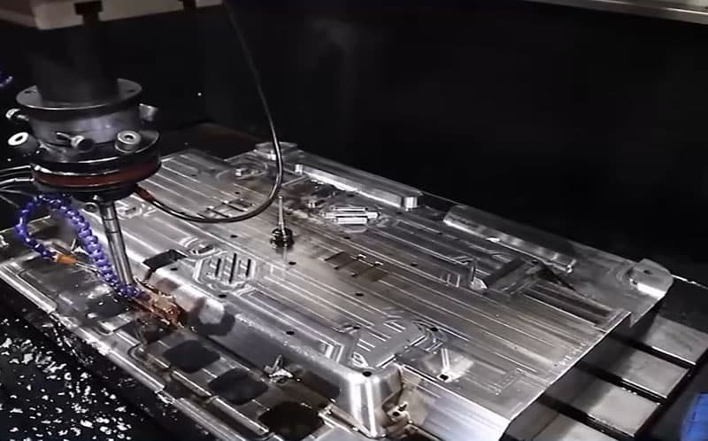 CNC machining of injection mold using 5-axis milling with coolant spray and metal shavings