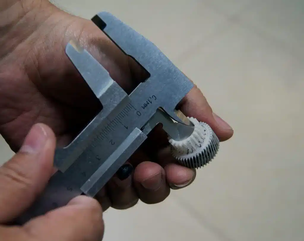 Measuring injection molded plastic gear using calipers to verify dimensional tolerance and accuracy
